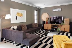 Moderne Polstercouch übereck und gelbe Tagesliege auf schwarz-weißem Teppich in Wohnzimmer, mit grau getönten Wänden