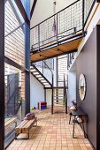 Rustic bench against glass facade and dark table against black wall in open-plan hallway of contemporary building with dog-leg stairs and bridge