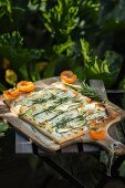 Courgette unleavened bread with goat's cream cheese, apricots and rosemary in front of a courgette bed