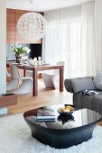 Black glossy coffee table on long-pile rug and designer lamp above dining dining and white Panton chairs