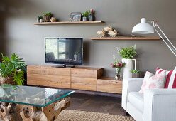 Coffee table with glass top, pale armchair and low sideboard with rustic, wooden cupboards on grey wall