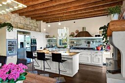 Bar stools at island counter in open-plan kitchen with wood-beamed ceiling