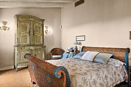 Wicker sleigh bed and antique carved wardrobe in rustic bedroom