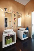 White, twin washstands with countertop basins, mirrors and motto painted on apricot wall