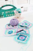 Patchwork-style, pastel crochet blanket being sewn together, crochet needle and ball of purple wool