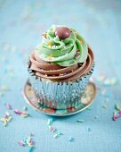 A cupcake with chocolate and lime frosting decorated with chocolate beans and sugar sprinkles