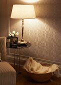 Lit table lamp on side table in front of geometric wallpaper