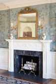 Elegant fireplace with stucco surround, romantic floral wallpaper, gilt-framed mirror and china pots arranged on mantelpiece