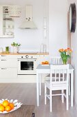 Small dining area with vase of tulips in open-plan kitchen; bowl of oranges on coffee table in foreground