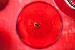 A view from above of a red drinking glass garnished with a cocktail tomato