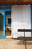 White curtain on open glass sliding door with blue frame leading to Mediterranean-style terrace