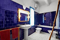 Glossy, ultramarine wall tiles in Mediterranean-style bathroom with bathtub, pedestal sink and bidet