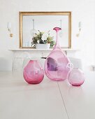 Round, pink glass vases on table in front of mirror above fireplace