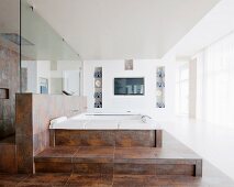 Large bathroom with whirlpool bath on platform covered in rust-effect tiles