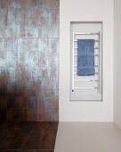 Heated towel rail in niche next to rust-effect tiles