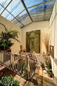 Mediterranean-style, sunny stairwell with glass roof, potted plants on floor and surfaces