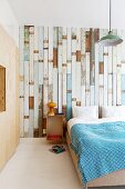 Bed against wallpaper with pattern of old floorboards and plywood fitted wardrobe to one side