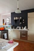 Pale, modern fitted cabinets and black-painted wall in open-plan kitchen area