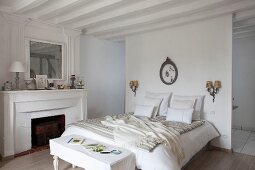White, rustic bedroom with open fireplace and ensuite bathroom behind partition