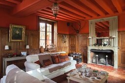 Seating area in front of fireplace in grand country house with half-height wood panelling and red-painted walls and ceiling
