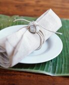 Linen napkin decorated with pebble on white plate on banana leaf used as place mat
