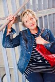 An older woman wearing a denim jacket and a striped top leaning on a barrier