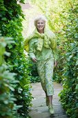 An older woman wearing a light green blouse and green-and-white trousers running in a garden