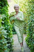 Ältere Frau mit hellgrüner Bluse und grün-weisser Hose läuft im Garten