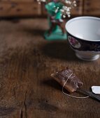 A used black tea bag on a wooden table in front of a tea cup