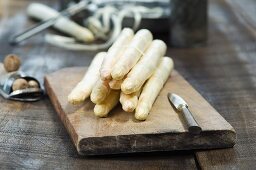 Frischer weisser Spargel auf Schneidebrett daneben Muskatreibe mit Muskatnüssen