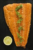 Geräucherter Lachs mit Dill vor schwarzem Hintergrund (Aufsicht)