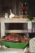 Roasted goose in a roasting dish with a glass of red wine next to it
