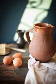 A rustic arrangement with a terracotta jug, eggs and butter