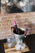 Bottle in wine cooler and tealights on wooden board in front of brick wall