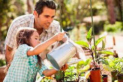 Vater und Tochter gießen die Topfpflanzen im Garten