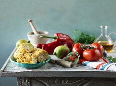 An arrangement featuring grilled corn cobs, tomatoes, peppers, lemons and oil