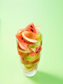 A glass of apple and melon slices on a light green surface