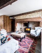 Antique white armchair and small ottoman in front of stone fireplace in rustic living room