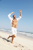 Junger Mann in Shorts und offenem Hemd läuft am Strand
