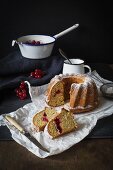 A sliced redcurrant Bundt cake dusted with icing sugar on a piece of white paper on a dark slate surface
