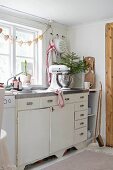 Mixer and vase of fir branches on festively decorated kitchen counter below garland of gingerbread hearts
