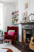 Red velvet armchair next to antique open fireplace decorated with fairy lights