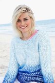 A blonde woman on a beach wearing a blue angora jumper