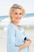 A blonde woman on a beach wearing a striped shirt and a light blue cardigan