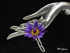 A silver hand with a chain and an exotic flower