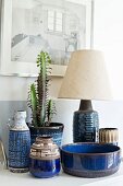 Blue, patterned ceramic containers and cactus in pot next to table lamp