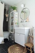 Schlichtes Waschtischmöbel unter rundem Spiegel an weiss gefliester Wand im Bad, Badewanne hinter Vorhang