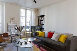Mehrteilige Couchtische mit amorpher Tischplatte und dunkelgraue Couch mit farbigen Kissen im Wohnzimmer