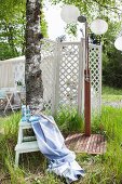 Regendusche im Freien, Badutensilien auf weißer Trittleiter vor Paravent im sommerlichen Garten