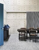 Esszimmer mit Betonwänden, dunklen Möbeln und einer blauen Tür